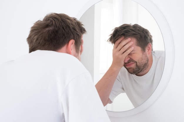 Photo tired mature caucasian man is looking at the mirror