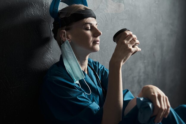 Tired medical worker doctor holding a paper cup of coffee after taking a large number of patients due to the epidemic of coronavirus