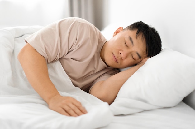 Tired middle aged asian man asleep resting peacefully in bed