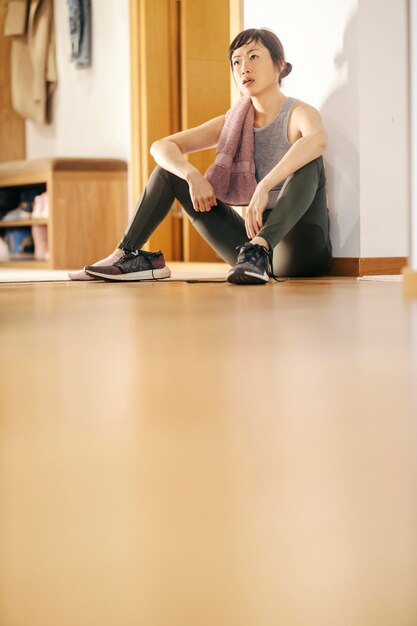 Photo a tired middle aged japanese sportswoman is sitting on a floor and taking a break
