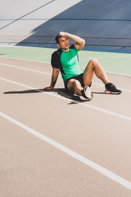 Tired mixed race sportsman sitting at stadium and touching head