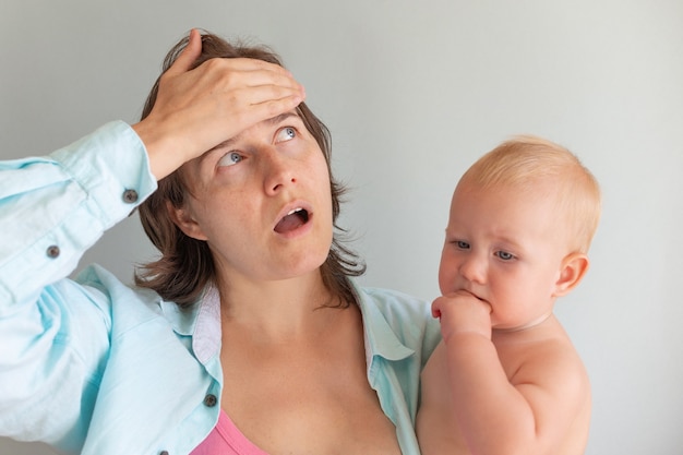 Tired mom trying to calm her crying infant baby on hands. Newborn tantrum. Motherhood concept. Depressed woman with child at home.