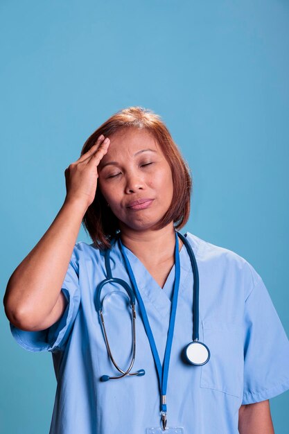 Photo tired nurse having migraine while working at medical expertise during checkup visit appointment, portrait. depressed sick assistant suffering from headache. health care service and concept