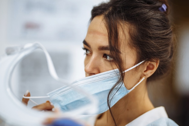 Tired nurse takes off a protective face shield and medical mask\
after a tough working shift at the hospital. female doctor fights\
the coronavirus pandemic working hard overtime and being\
exhausted.