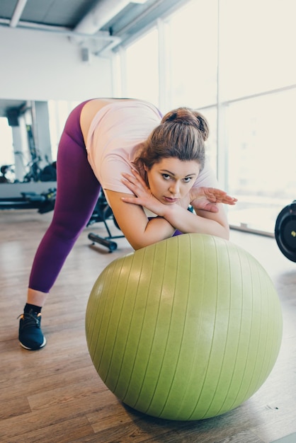 Tired Obese Woman Leans on gym ball in gym