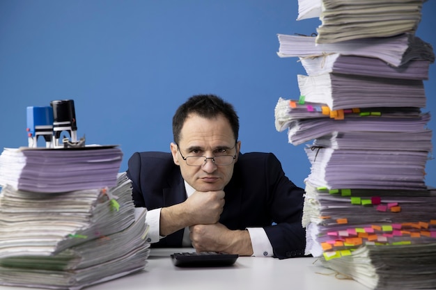 Tired office worker puts his head on his fists, surrounded by high stacks of documents