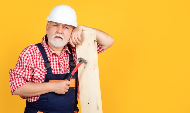 Tired old man woodworker in helmet on yellow background