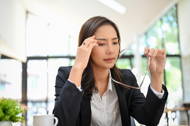 피곤하고 과로한 아시아 여성 사업가가 책상에서 일하는 동안 안경을 벗었다