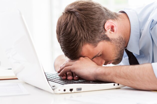 Tired and overworked. Side view of young man in shirt and tie sleeping while sitting at his working place