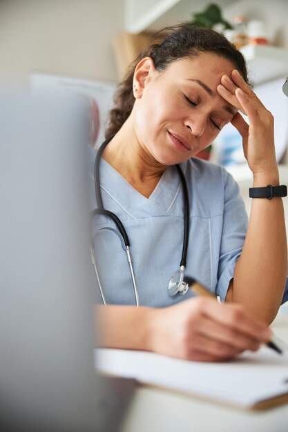 Tired physician grabbing her head while using a pen