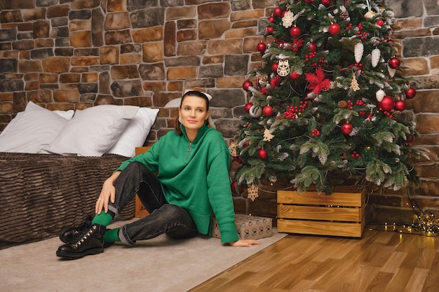 Photo tired but positive mom sits on the floor after finishing decorating the christmas tree