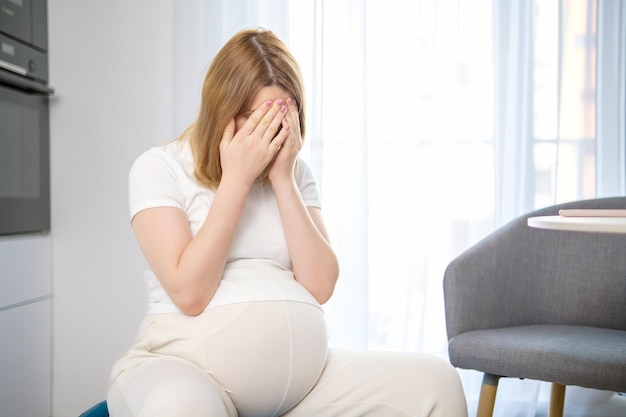 Tired pregnant woman closes her face with her hands