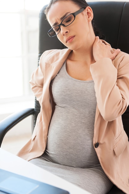 Tired pregnant woman. Depressed pregnant businesswoman holding head in hand while sitting at her working place in office