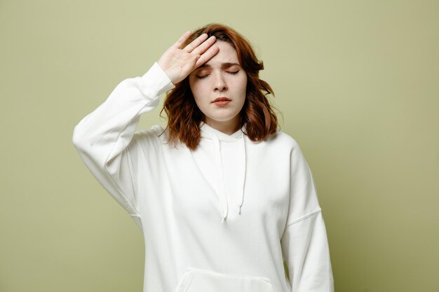 Tired putting hand on forehead young female wearing white sweater isolated on green background