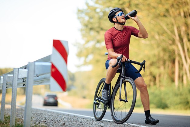 Photo tired road cyclist in black helmet and mirrored glasses refreshing with cold water