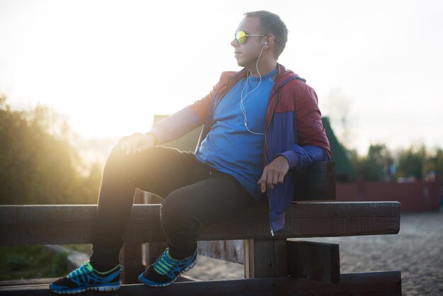 Tired runner sitting relaxing and listening to music your phone on a wooden pier sport