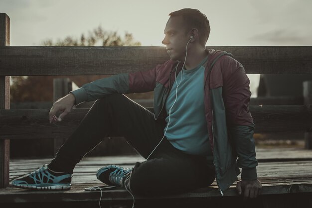 Tired runner sitting relaxing and listening to music your phone on a wooden pier sport