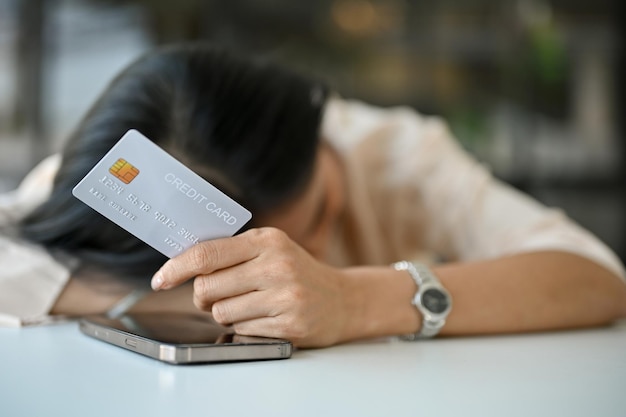 Photo tired and sad asian woman laid her head down on the table holding a credit card