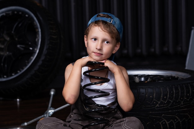 Tired sad child in the garage among the tires and wheels holding a spring shock absorber