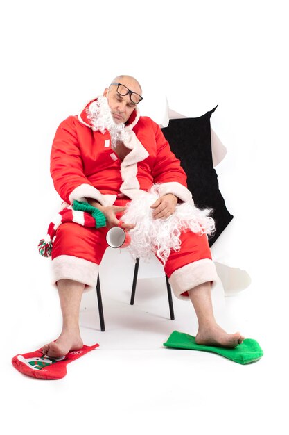 Foto babbo natale stanco un uomo con un costume rosso di natale dorme su una sedia su uno sfondo bianco