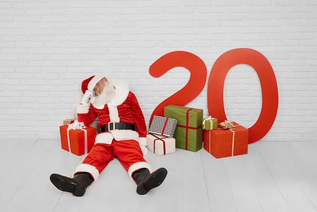 Tired Santa Claus sitting on the floor near red big gift box