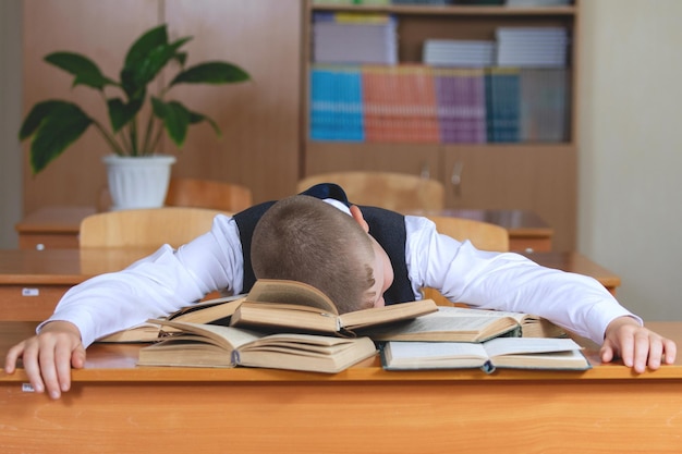 Lo scolaro stanco dorme alla sua scrivania, su una pila di libri.