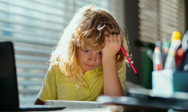 Tired schoolboy while doing homework concentrated child writing in notebook focused schoolboy studyi