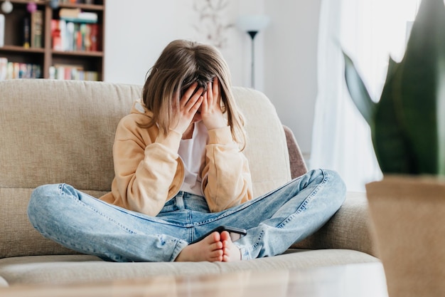 Tired schoolgirl girl sits on the couch and holds on with her hands per head childrens stress