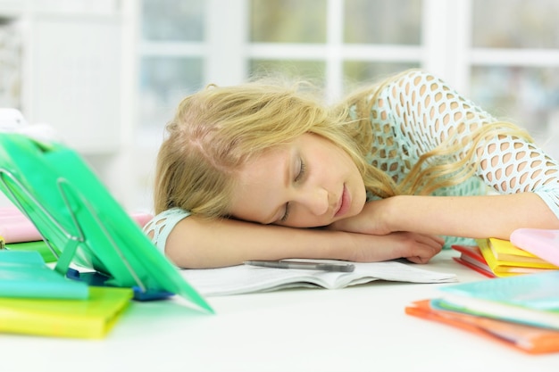 Tired schoolgirl sleeping at desk after studying