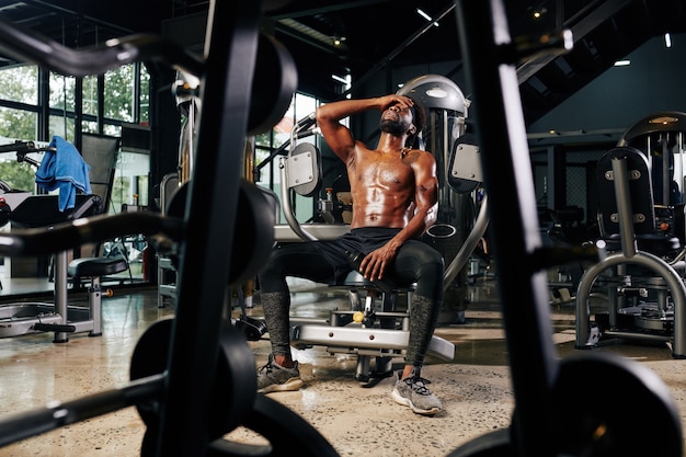 Tired shirtless sportsman resting in gym machine