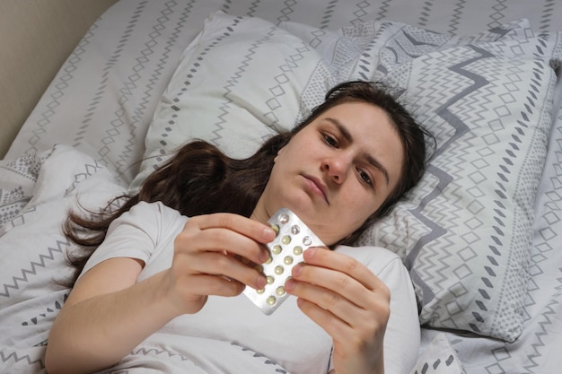 A tired sleepy woman lies in bed pills in her hands