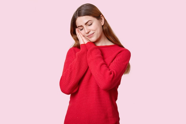 La donna assonnata stanca fa un pisolino appoggiato sui palmi delle mani, ha gli occhi chiusi, vestita di maglione rosso, vuole riposare, gode di un'atmosfera calma, isolata su rosa. persone, relax e sonno