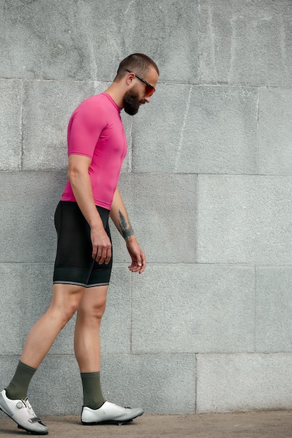 Tired sportsman in pink sportwear resting after an workout while standing against cement wall background with copy space area for text message or advertising man runner taking break after run