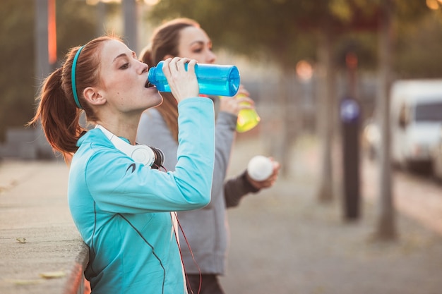 Tired sportswomen drinking water