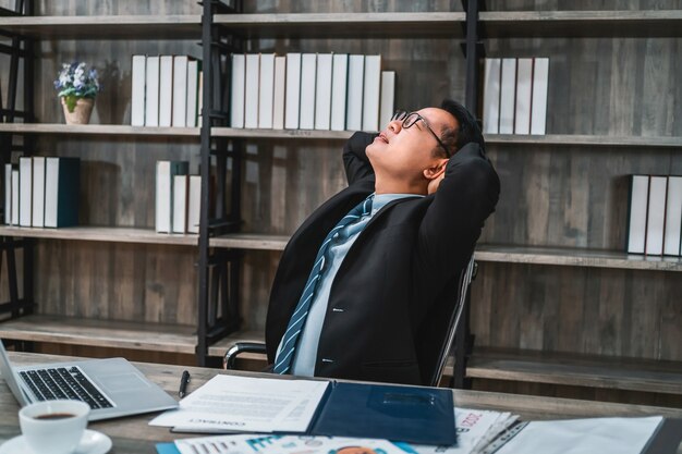Усталый напряженный деловой человек, страдающий от боли в шее, работает в офисе, сидя за столом