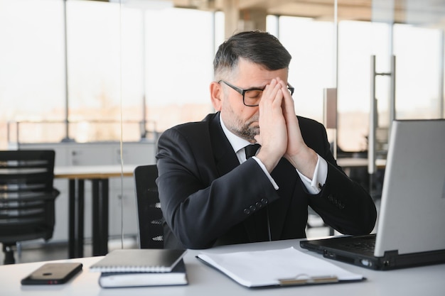 疲れたストレスを感じた会社員が机に座り、目をこすり、疲れ果てていると思っている