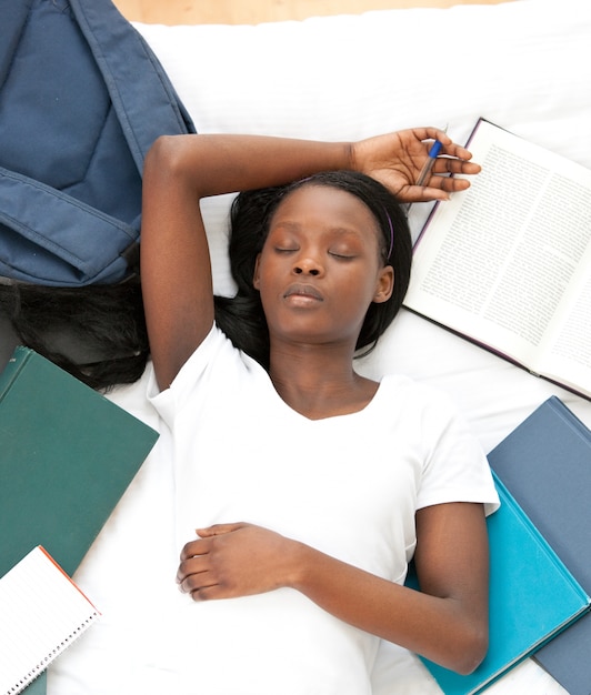 Tired student doing her homework lying on a bed