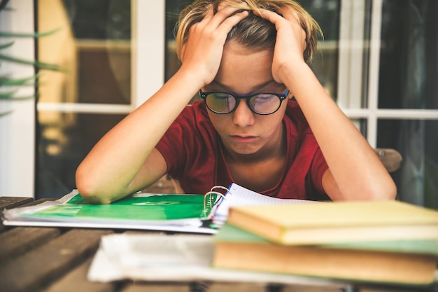 Foto studente stanco che fa i compiti a casa seduto all'aperto con libri scolastici e giornali ragazzo stanco