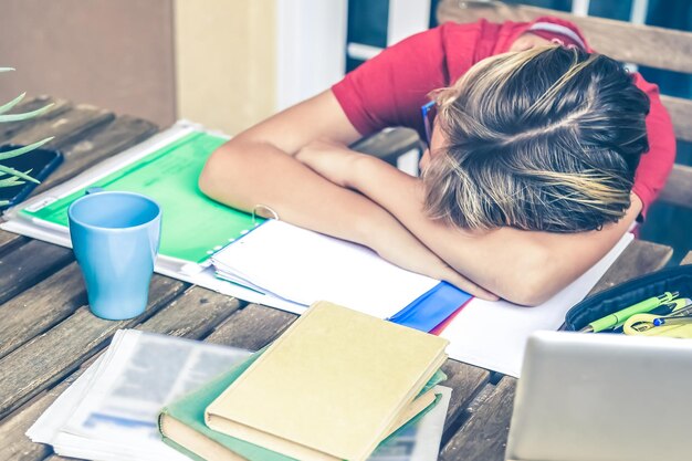 Photo tired student doing homework at home with school books and newspaper boy weary due to heavy study