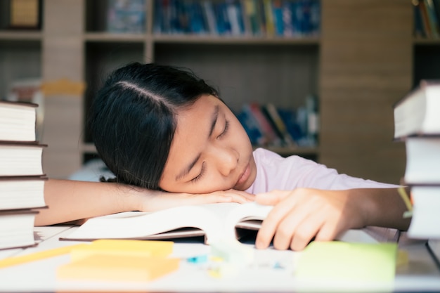 Tired student girl with books sleeping on the table. 