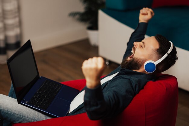 Studente stanco con le cuffie si siede sulla poltrona rossa e sbadiglia dopo aver studiato online.