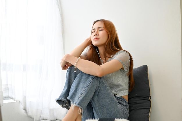 Tired and unhappy millennial Asian woman sitting in living room feeling upset with herself