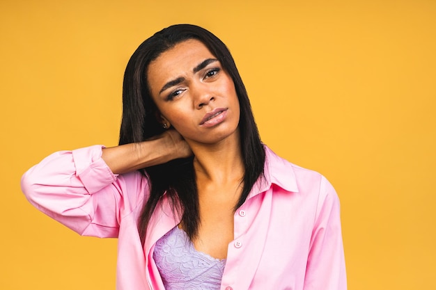 Tired upset african american woman massaging hurt stiff neck\
isolated over yellow background fatigued sad black lady rubbing\
tensed muscles to relieve joint shoulder pain fibromyalgia\
concept