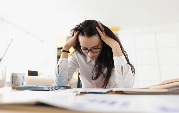 疲れた女性は文書を持った机の上に頭を下ろしました