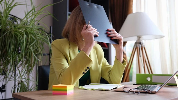 Photo tired woman covers face with folder of documents bad working mood mood and fatigue concept