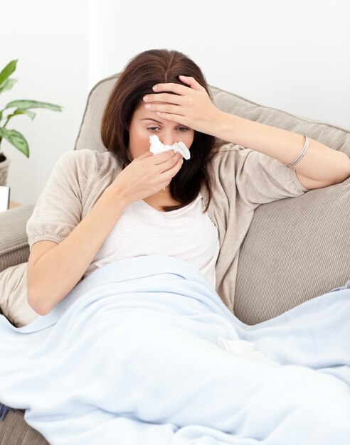 Tired woman feeling her temperature while blowing her nose