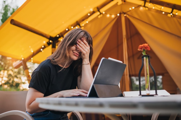 Tired Woman freelancer using a laptop on a cozy glamping tent in a sunny day Luxury camping tent for outdoor summer holiday and vacation Lifestyle concept