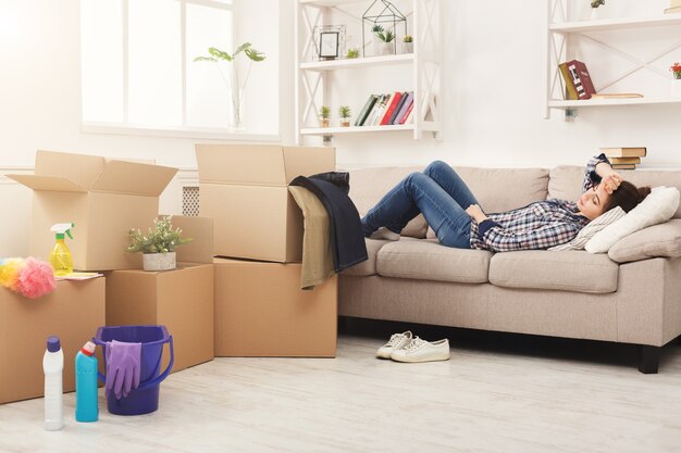 Tired woman having rest after cleaning home, lying on sofa in the living-room, copy space. Housekeeping and home cleaning concept