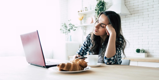 写真 疲れた女性がキッチンのノートパソコンの近くで寝ています