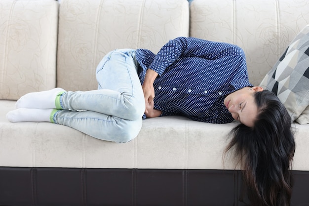 피곤한 여성은 여성 개념의 하복부에 복통이 있는 소파에 누워 있다